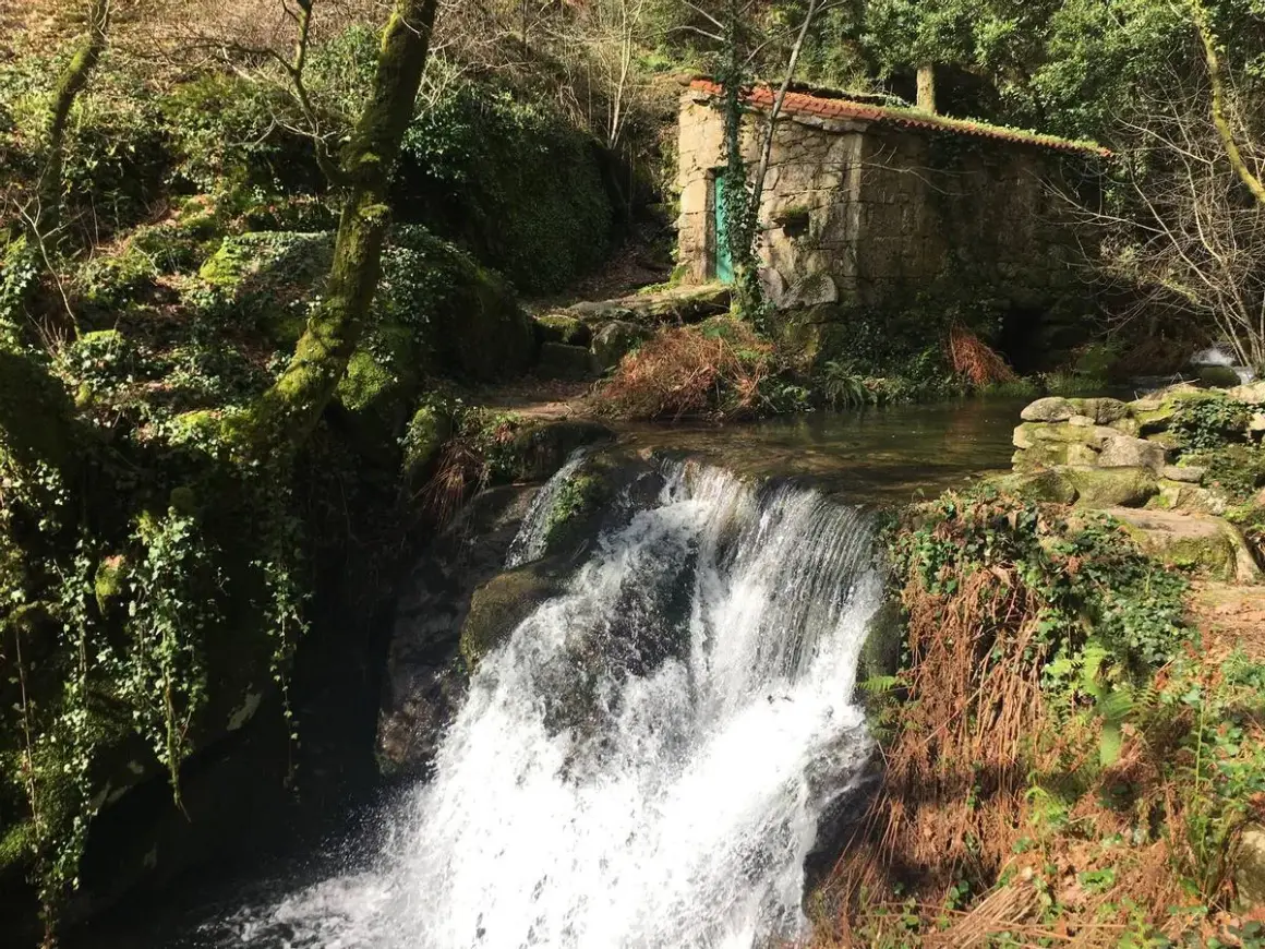 Cascada en el parque natural Monte Aloia, con una pequeña casa de piedra y vegetación exuberante.