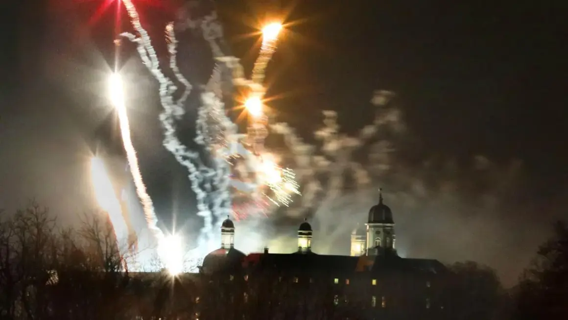 Feuerwerk über Bergisch Gladbach. Farbenfrohe Raketen erleuchten den Nachthimmel über einem historischen Gebäude mit Kuppeln.