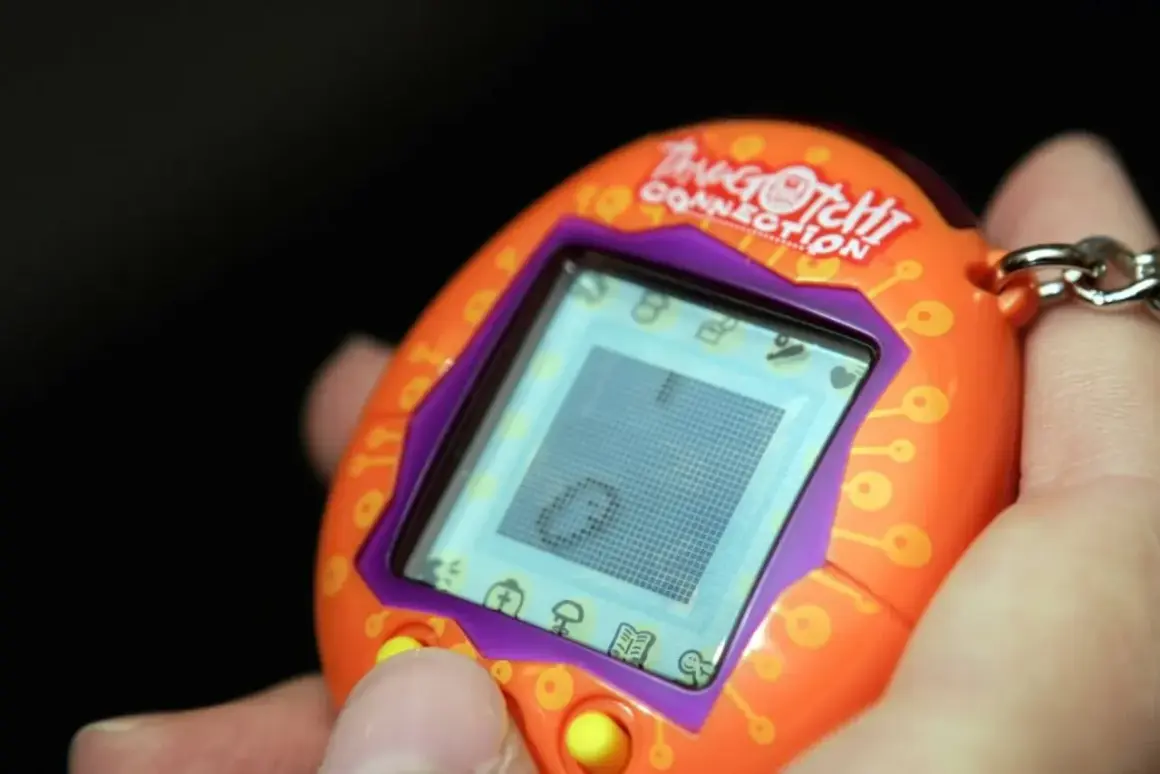Pomarańczowe Tamagotchi Connection w dłoni, z widocznym ekranem i przyciskami. Pamiętasz, co to tamagotchi?