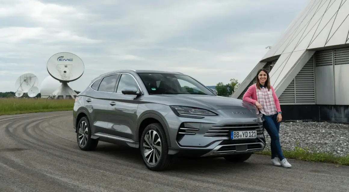 Mujer sonríe junto a un BYD Seal U, disfrutando del dm-i comfort en un día nublado, con antenas parabólicas de fondo.