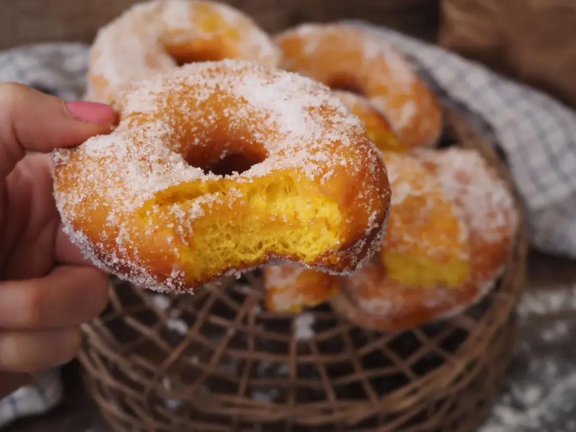 En hand håller en sockerdränkt munk, perfekt för ett hembakat donuts recept.