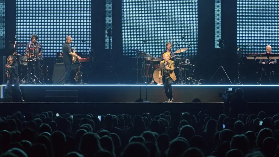 Ein Musiker mit goldenem Sakko singt auf der Bühne, umgeben von seiner Band. Ein Konzert von Simply Red in Stuttgart.
