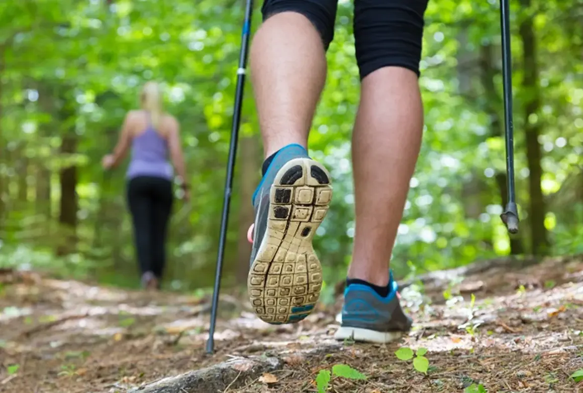 Osoba w bucikach na kijki nordic walking stawia krok na leśnej ścieżce.