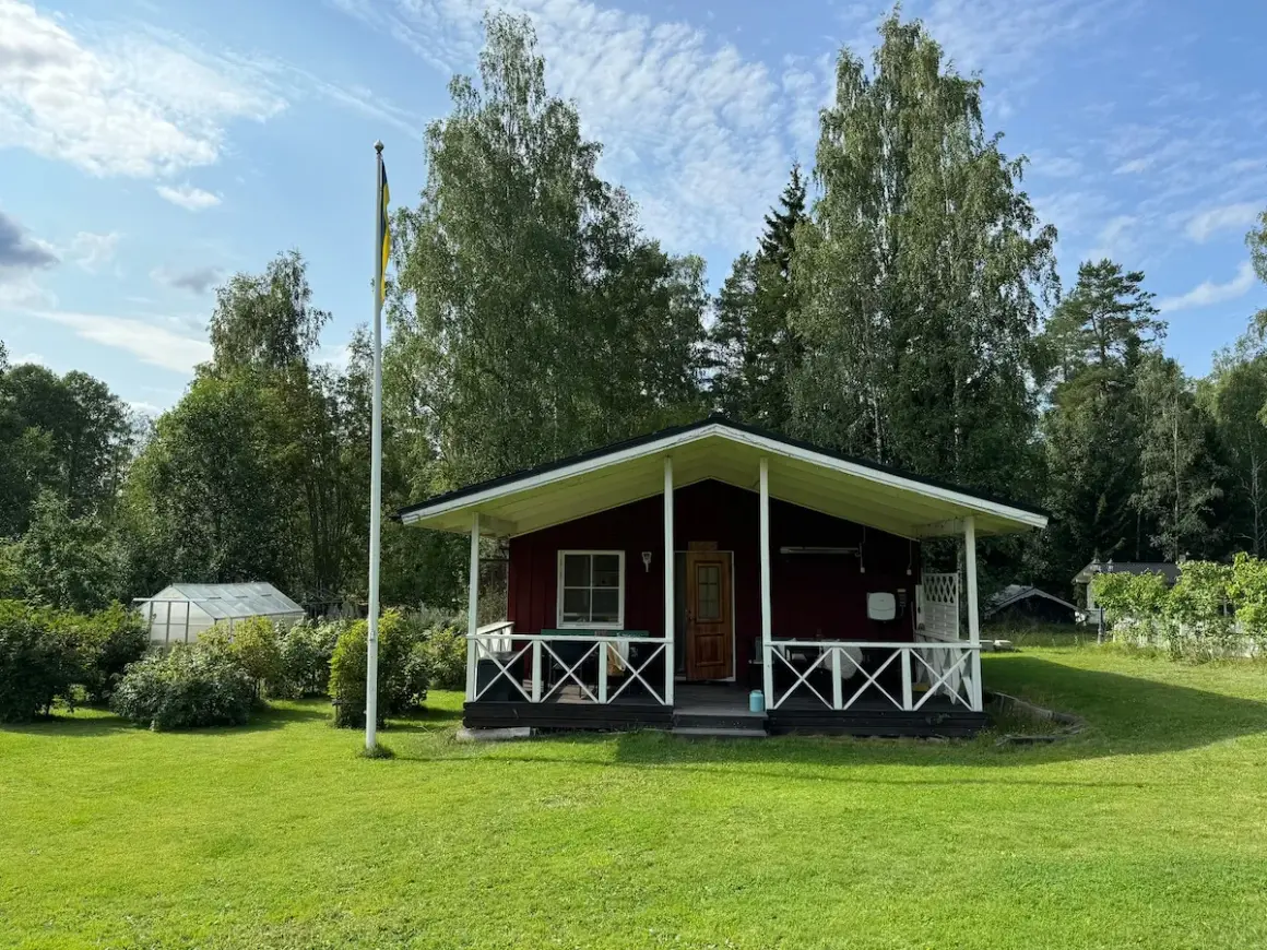 Rött hus med veranda och flaggstång i Stjärnsund. En växthus syns i bakgrunden.