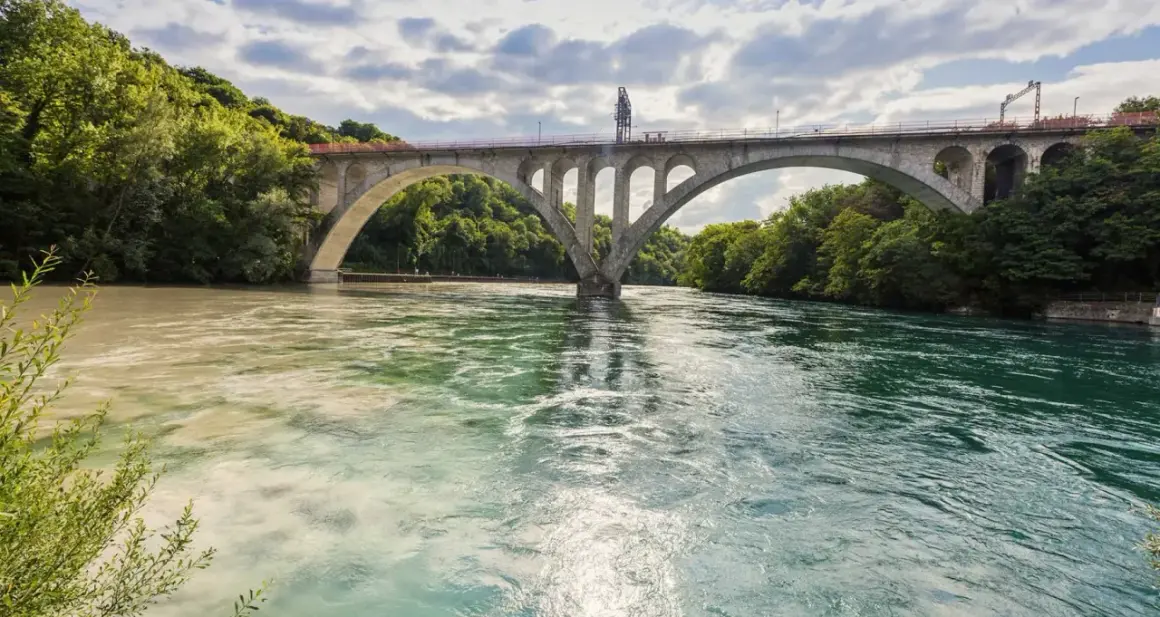 Ponte ad arco su fiume con acque di colori diversi, dove si intravedono segnali navigazione fluviale.