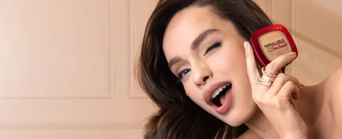 Uśmiechnięta kobieta prezentuje puder L'Oréal Infallible 24H Fresh Wear.