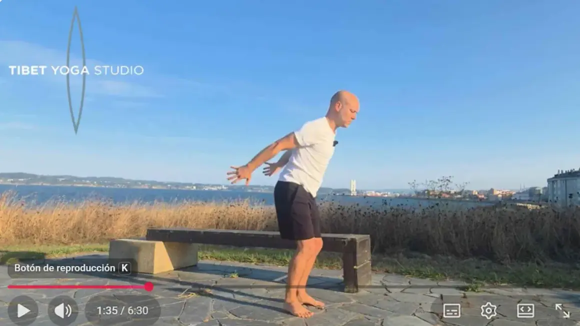 Hombre practicando yoga tibetano al aire libre, con el mar y la ciudad de fondo.
