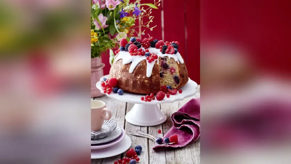 Ein köstlicher Gugelhupf mit Mandeln, Beeren und Zuckerguss, dekoriert mit frischen Früchten.