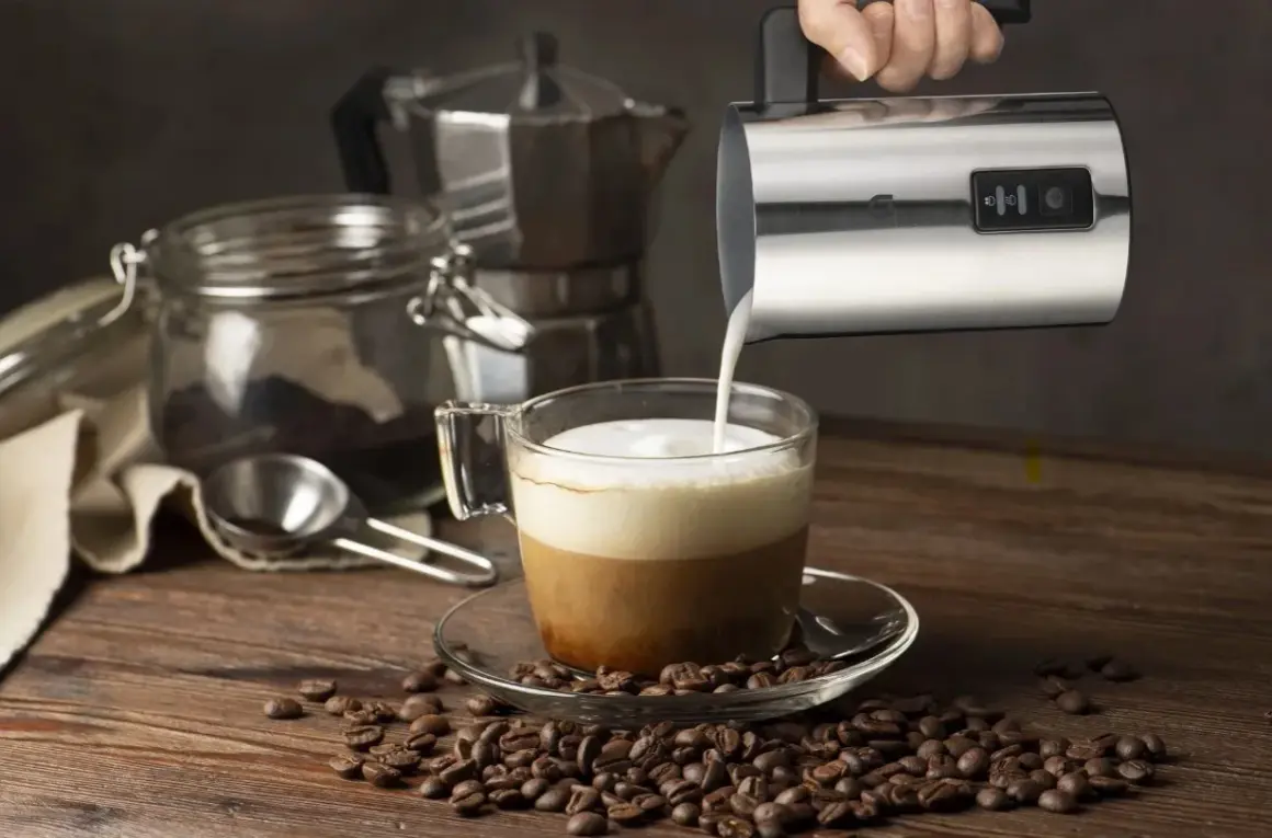 En hand häller mjölkskum i en kaffekopp, redo för ett perfekt kaffe recept. Kaffebönor sprider sig över träbordet.