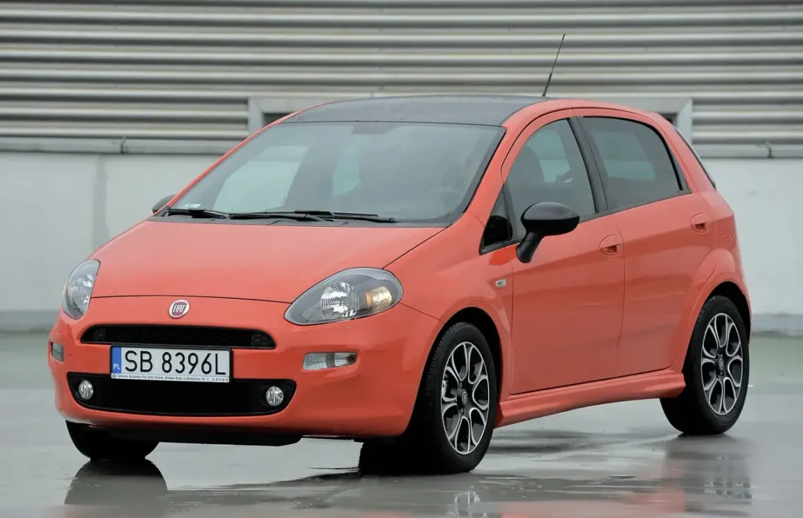 Pomarańczowy Fiat Punto na mokrej nawierzchni. Zwróć uwagę na jego kompaktowe fiat punto wymiary, idealne do miasta.