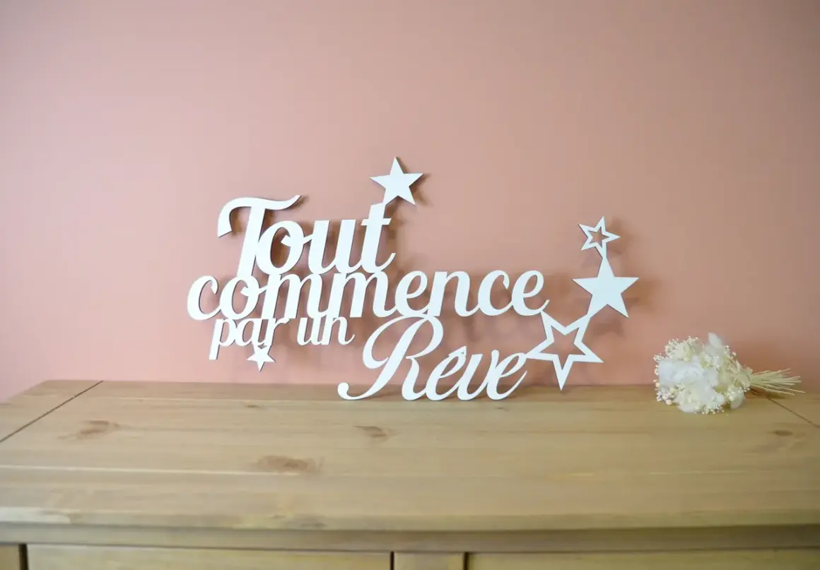 Une **lettre en bois blanc** forme la phrase "Tout commence par un Rêve", ornée d'étoiles. Un petit bouquet de fleurs séchées est posé à droite.