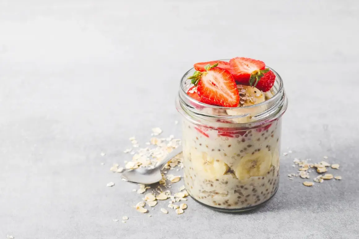 En burk med overnight oats recept toppad med jordgubbar och banan. Havregryn och en sked ligger bredvid.