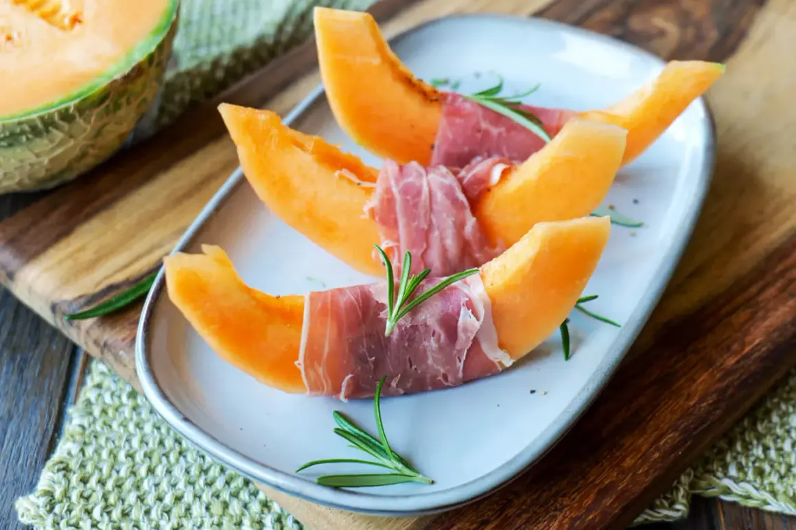 Melone mit Schinken, garniert mit Rosmarin, auf einem Teller. Ein Klassiker, der süße und salzige Aromen vereint.