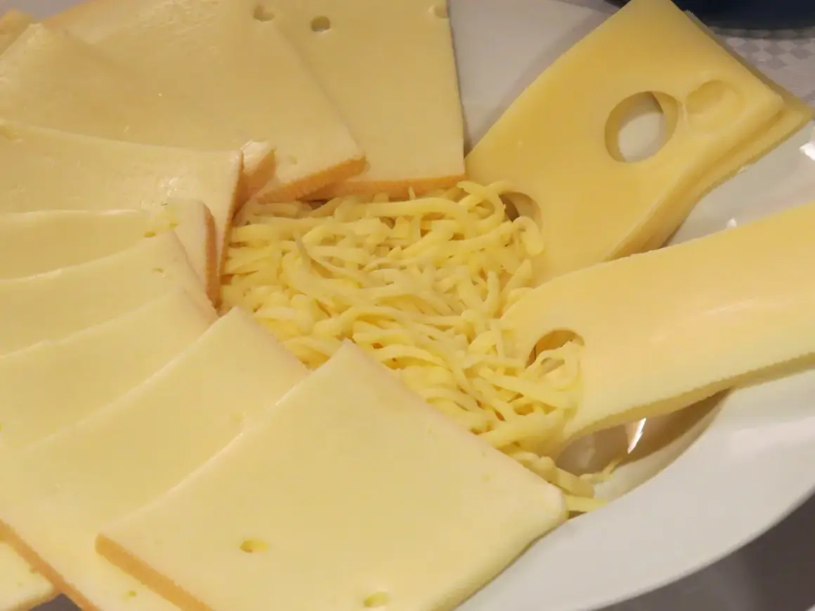 Assiette de fromages variés, dont des tranches d'Emmental avec ses trous caractéristiques, et du Gruyère râpé. La différence entre gruyère et emmental est subtile.