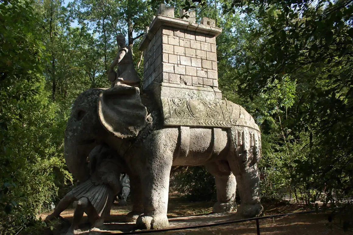 Elefante di pietra con guerriero e torre nel viterbo giardino dei mostri. Un'antica creatura che emerge dal verde.