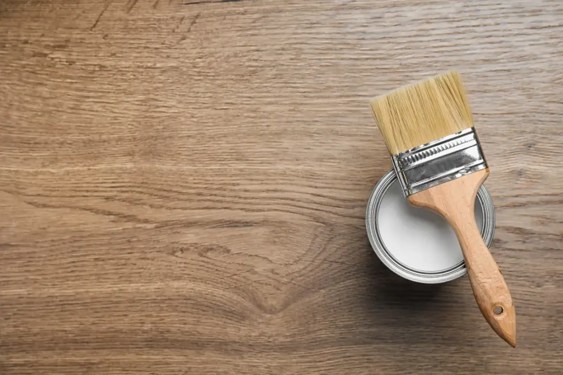 Pennello e barattolo di vernice bianca pronti per colorare legno su una superficie di legno grezzo.
