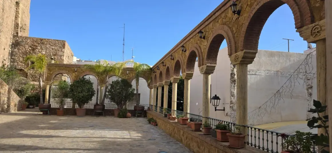 Un patio con arcos de piedra y columnas, palmeras y plantas en macetas. Un lugar encantador que ver en Vera, con un cielo azul despejado.