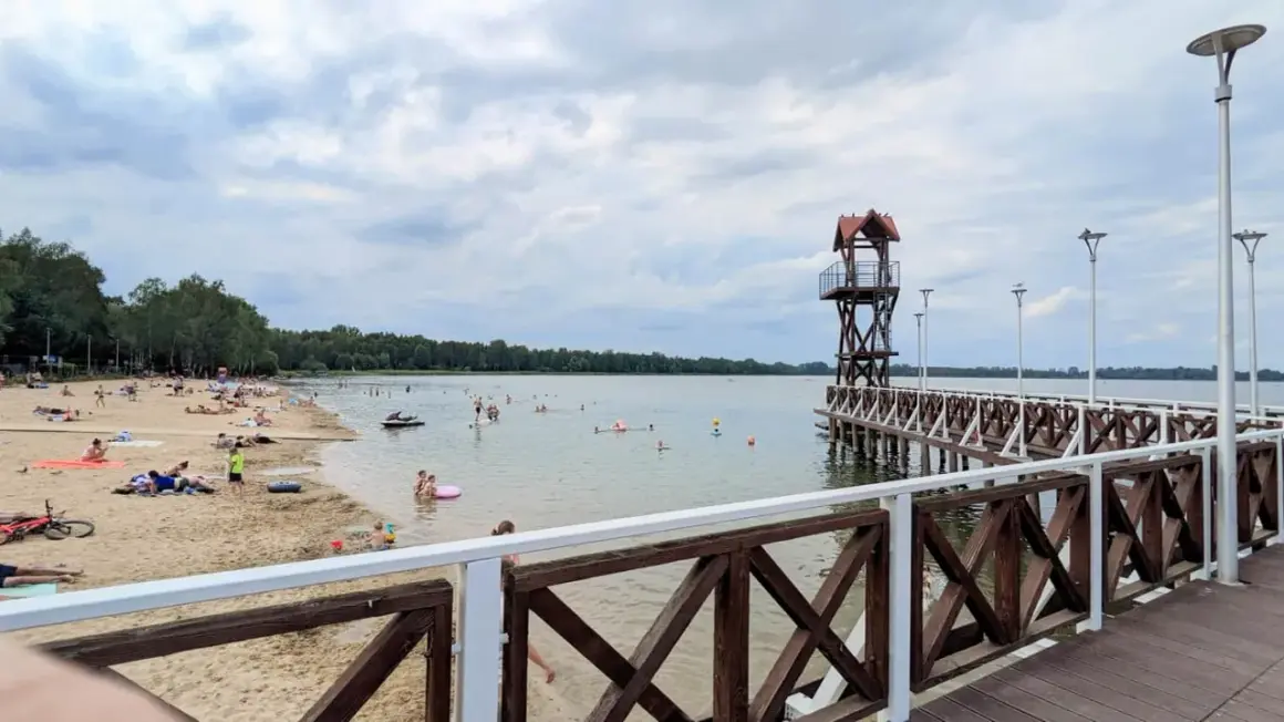 Plaża z ludźmi, pomost z wieżą ratowniczą i jezioro w Pogorii.
