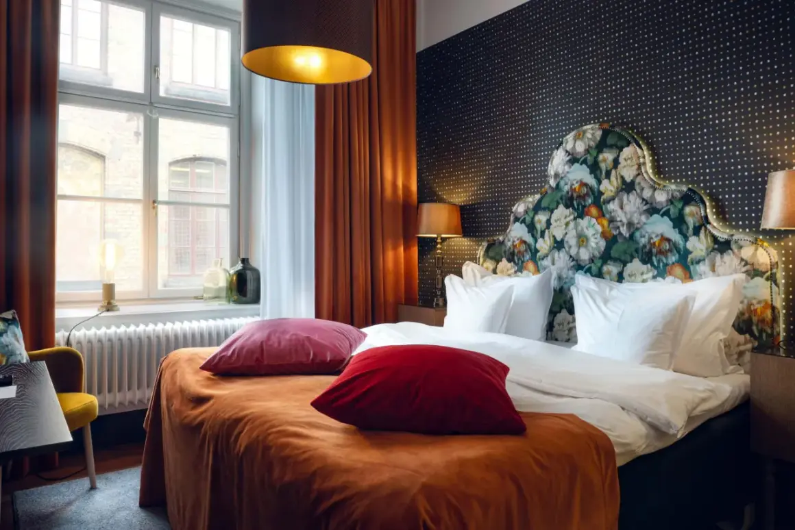 Ett lyxigt rum på nofo hotell Stockholm med en stor säng, blommig huvudgavel och orangea sammetsgardiner.