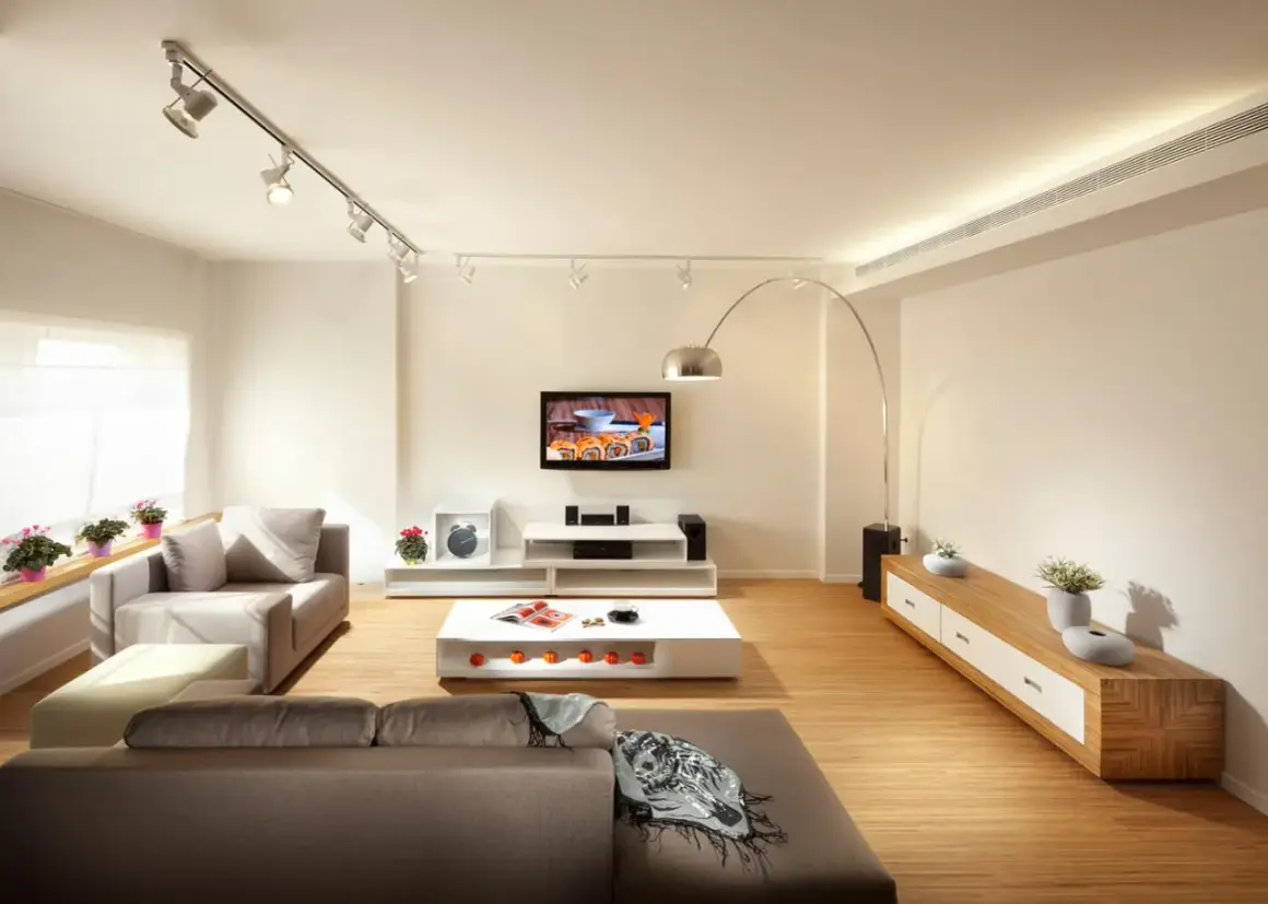 Iluminar un salón moderno con focos dirigibles y una lámpara de arco. Sofás grises, mesa de centro blanca y mueble de TV.
