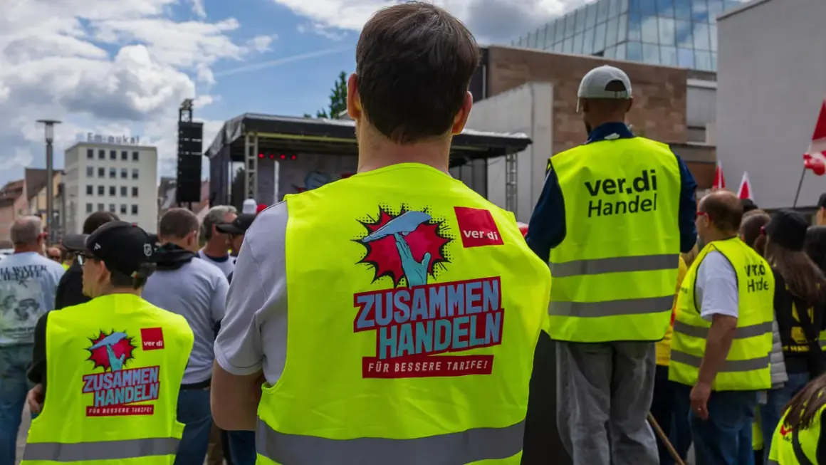 Menschen in Warnwesten mit der Aufschrift "ZUSAMMEN HANDELN FÜR BESSERE TARIFE!" bei Tarifverhandlungen im Einzelhandel.