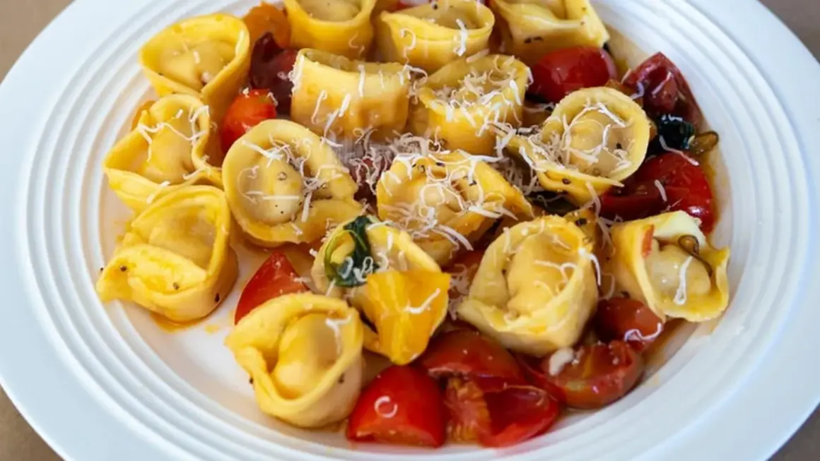 Talerz pełen tortellini z pomidorkami koktajlowymi i startym parmezanem.