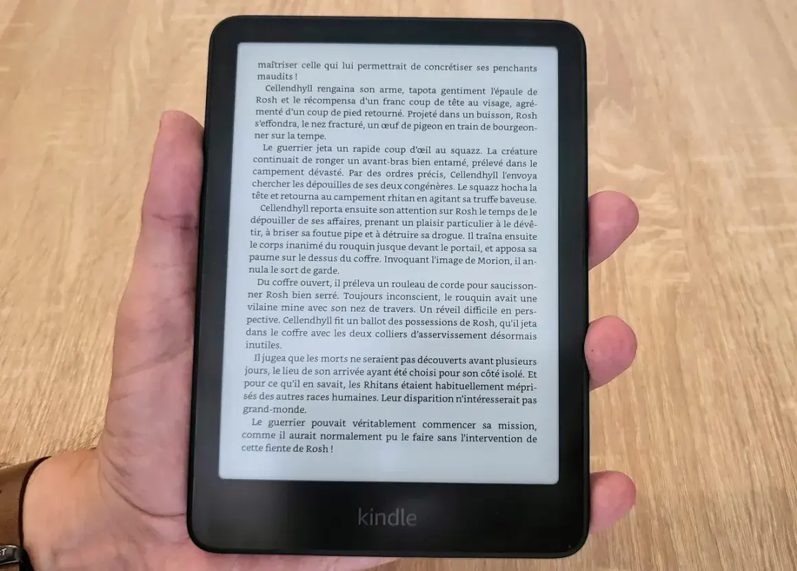 Main tenant un appareil Kindle format e-reader, affichant un texte en français sur fond noir.