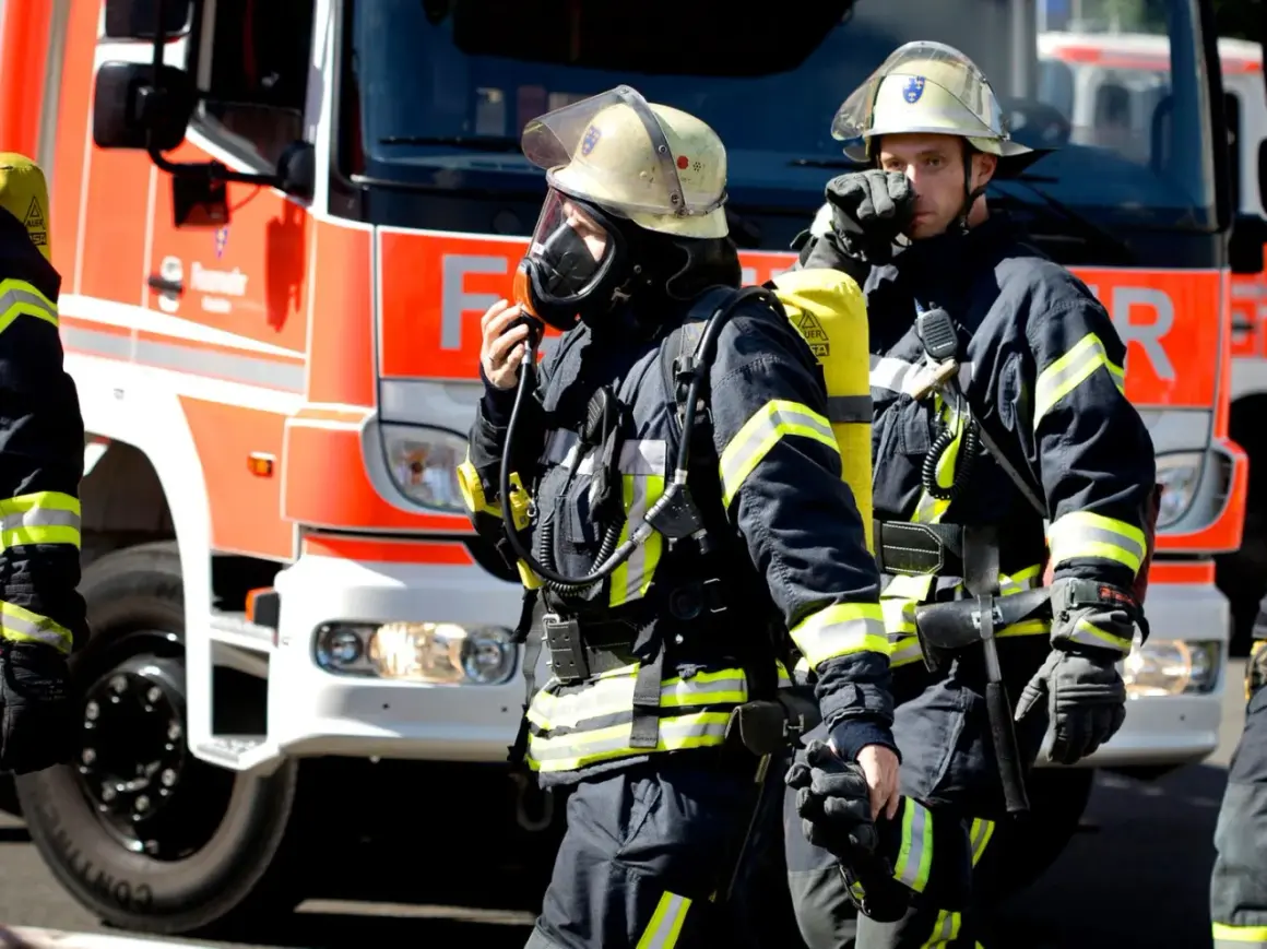 Zwei Feuerwehrmänner in voller Montur vor einem roten Feuerwehrauto. Sie sind bereit für den Einsatz. Wie viel verdient man als Feuerwehrmann?