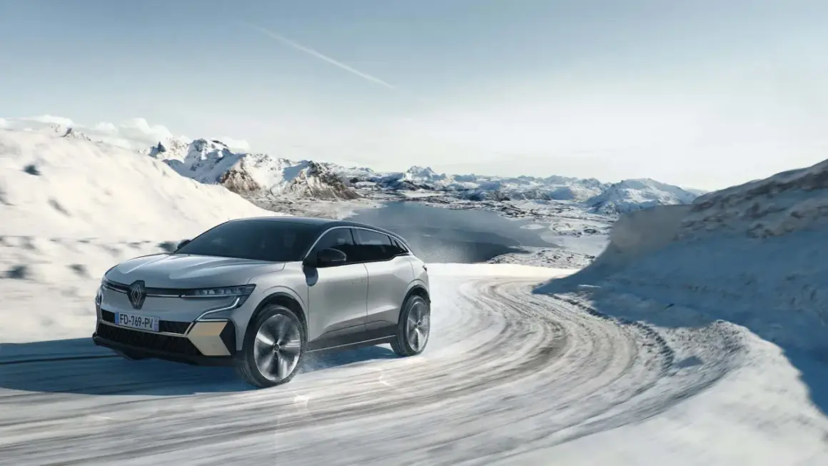 Voiture électrique avec pompe à chaleur traversant un paysage hivernal enneigé, montagnes et lac gelé en arrière-plan.