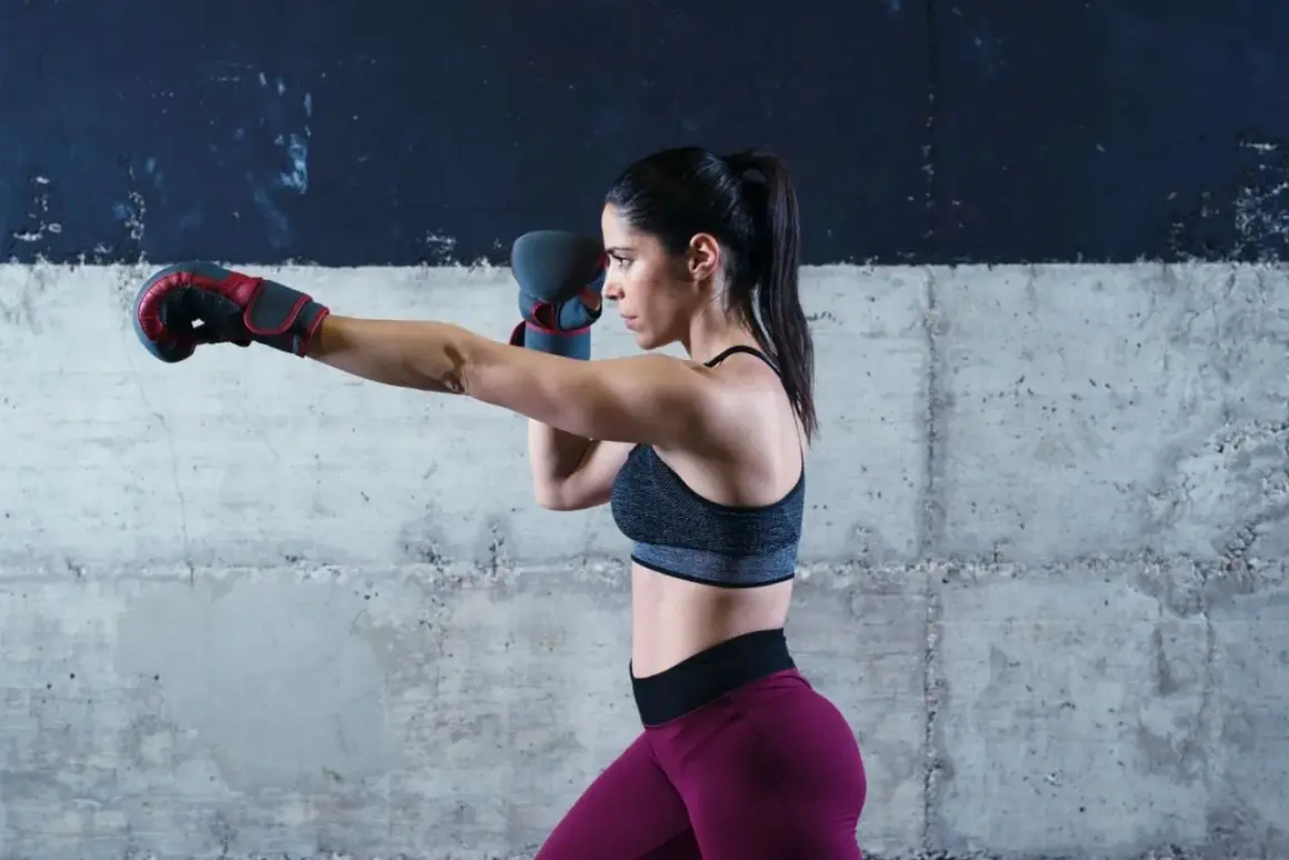 Woman in boxing gloves sparring, throwing a punch. Her focus is intense as she trains in a gritty, industrial-style gym.