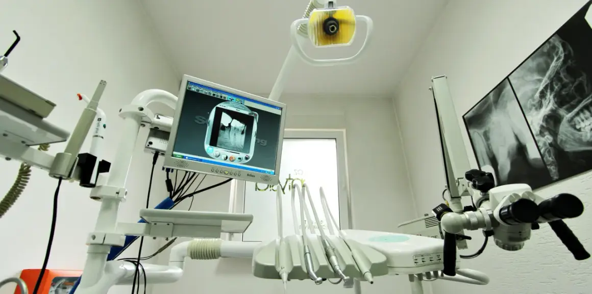 Nowoczesny gabinet stomatologiczny z aparaturą RTG i monitorem wyświetlającym zdjęcie zęba. NZOZ to skrót od Niepubliczny Zakład Opieki Zdrowotnej.