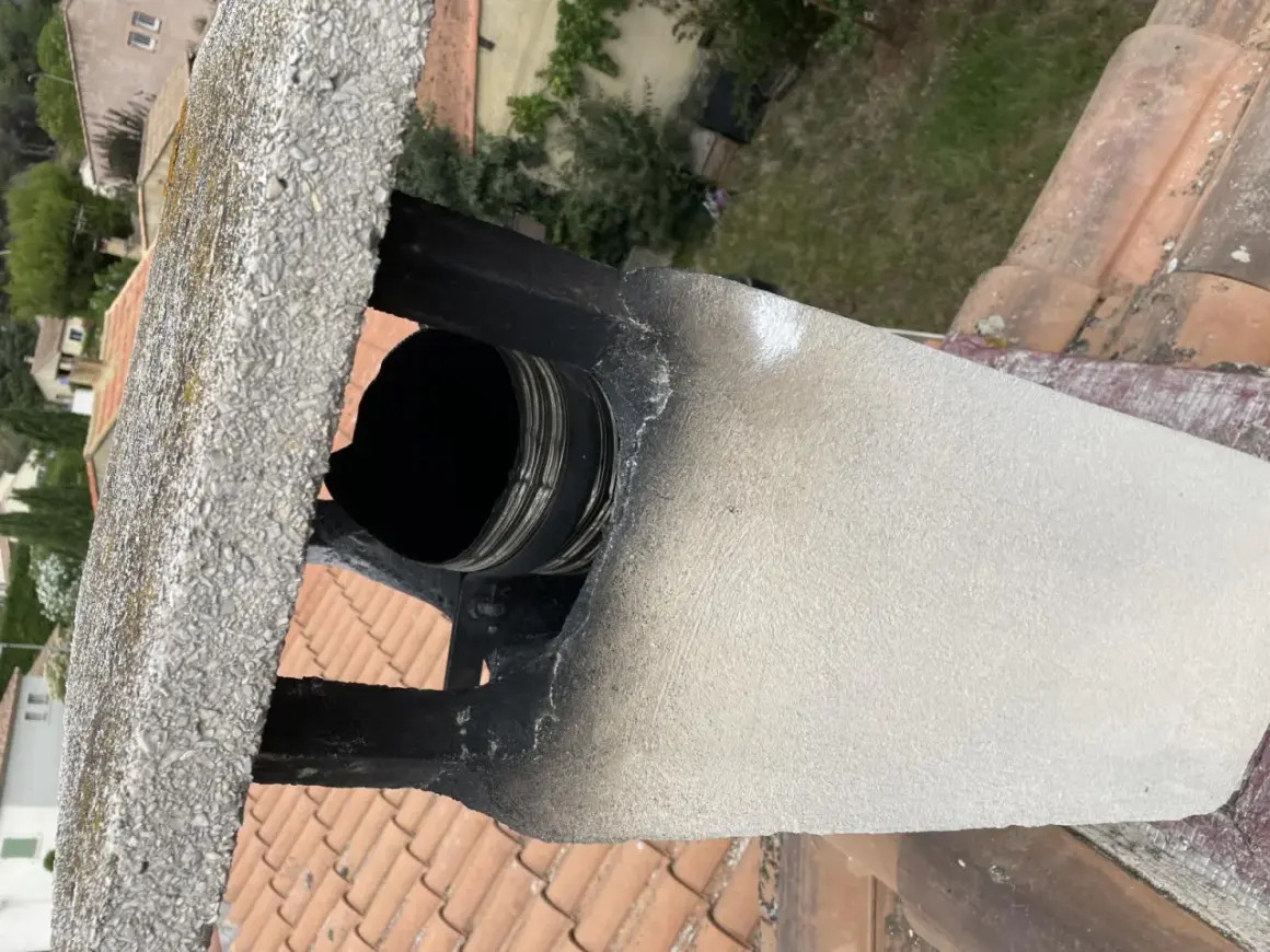 Détail d'un conduit de cheminée en métal noir, visiblement endommagé et encrassé, suggérant la nécessité de comment condamner un conduit de cheminée pour des raisons de sécurité.