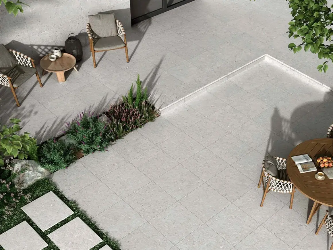 Terraza moderna con mobiliario de exterior y vegetación. El suelo está cubierto por un elegante **azulejo rectificado** de tonos grises, creando un espacio acogedor.