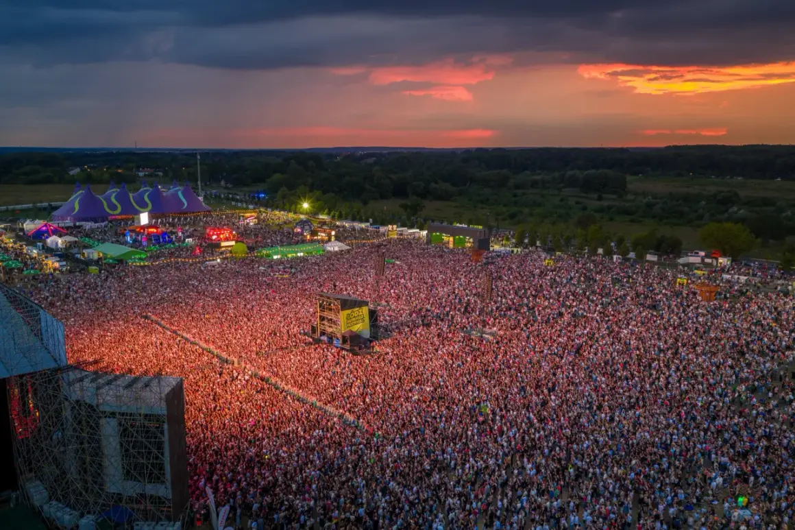 Widok z lotu ptaka na festiwal muzyczny z tłumem ludzi i sceną podczas zachodu słońca.