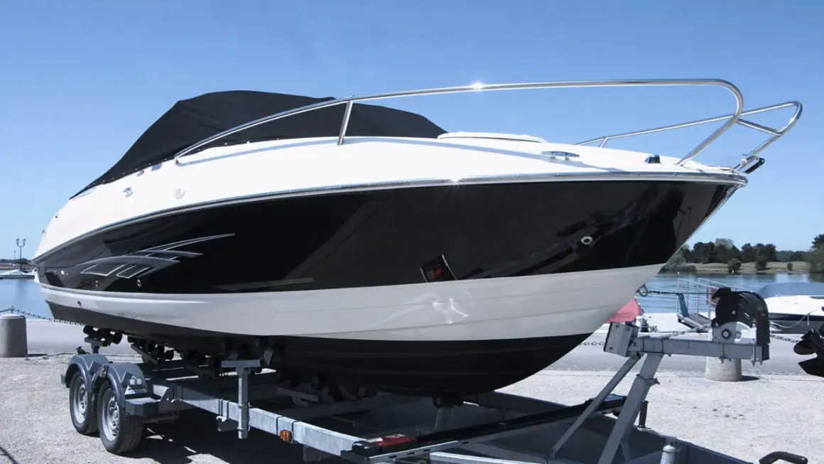 Barca sportiva bianca e nera su carrello, pronta per il varo. I candelieri sono i supporti metallici che la tengono ferma.