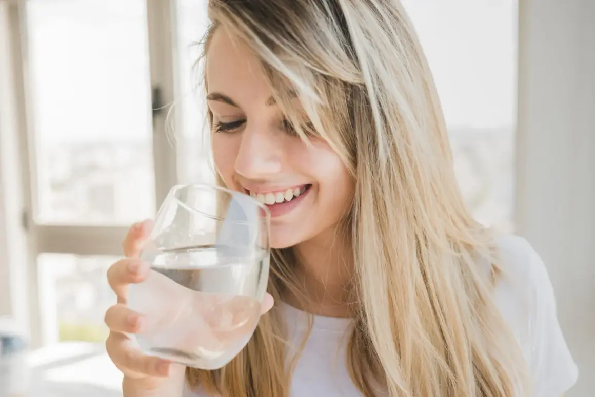 Une jeune femme souriante boit de l'eau osmosée dans un verre.