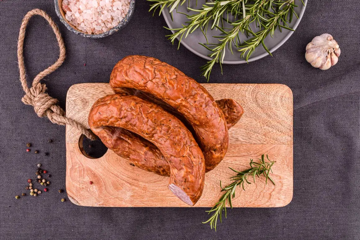 Wędzona kiełbasa na desce z rozmarynem, solą i pieprzem.