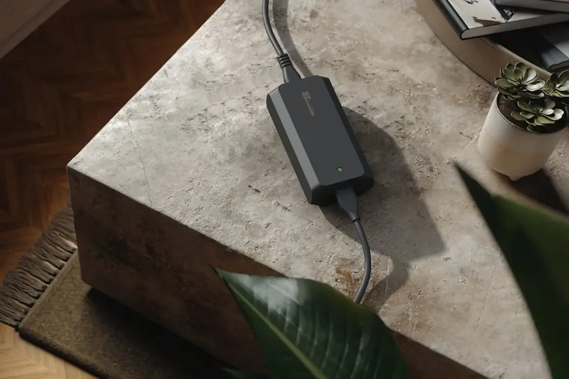 Chargeur noir avec une lumière verte allumée, posé sur une table en pierre. La question "peut on charger une batterie 4ah avec un chargeur 2ah" est soulevée par cet appareil.