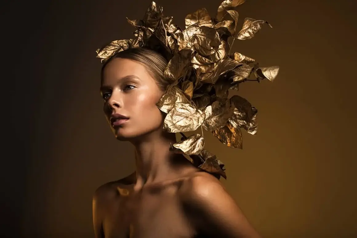 A model with a golden leaf headdress, captured with dramatic fashion lighting photography, showcasing a radiant glow.
