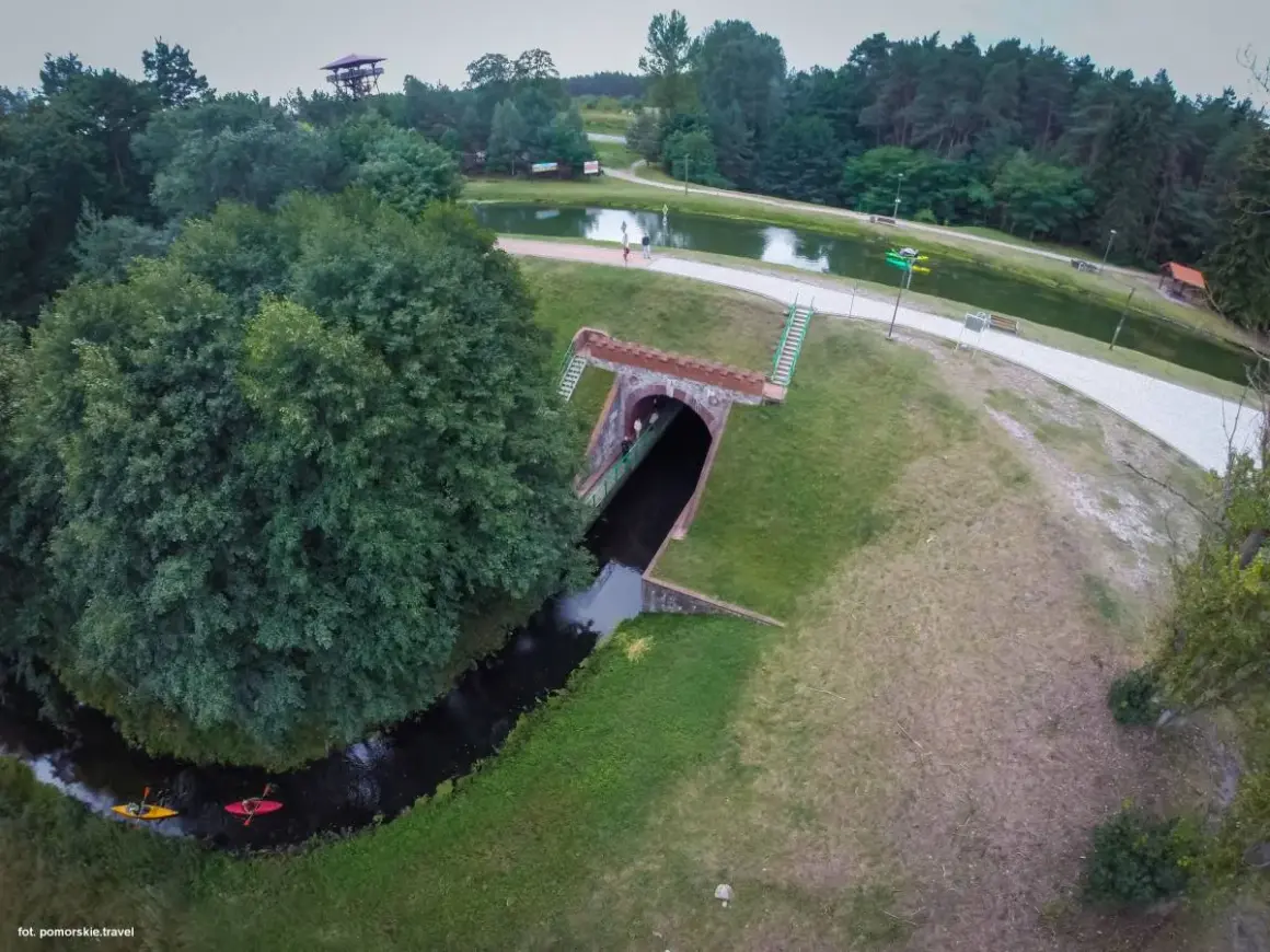 Akwedukt w Fojutowie, gdzie rzeka przepływa pod ziemią, a nad nią rozciąga się malowniczy park z jeziorem i wieżą widokową.