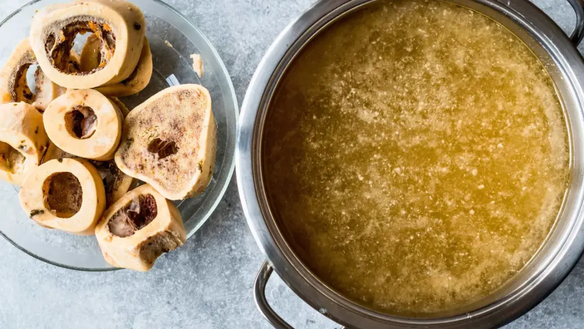 Un plato con huesos de tuétano y una olla con caldo dorado, perfecto para preparar caldo de huesos para perros.
