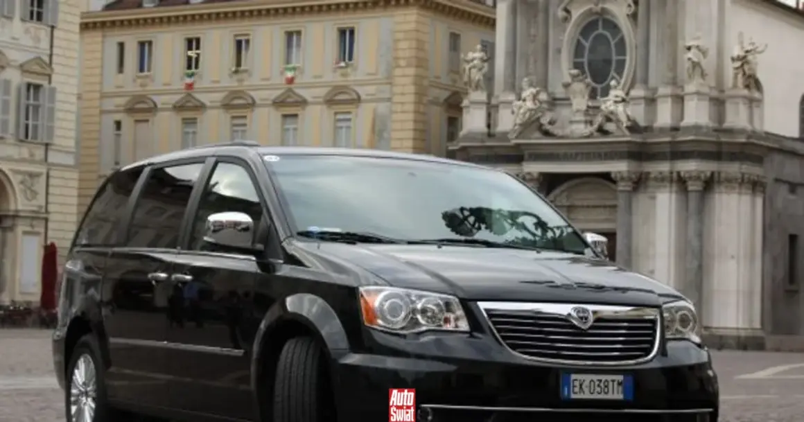 Czarny Lancia Voyager na tle zabytkowej architektury.