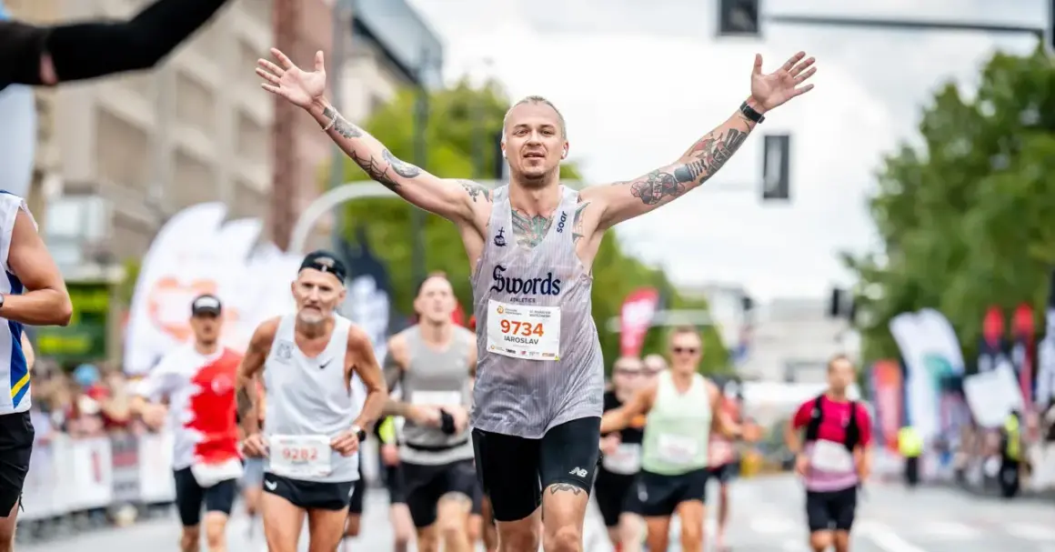 Triumfujący biegacz z tatuażami, z rękami w górze, na maratonie poniżej 2h.