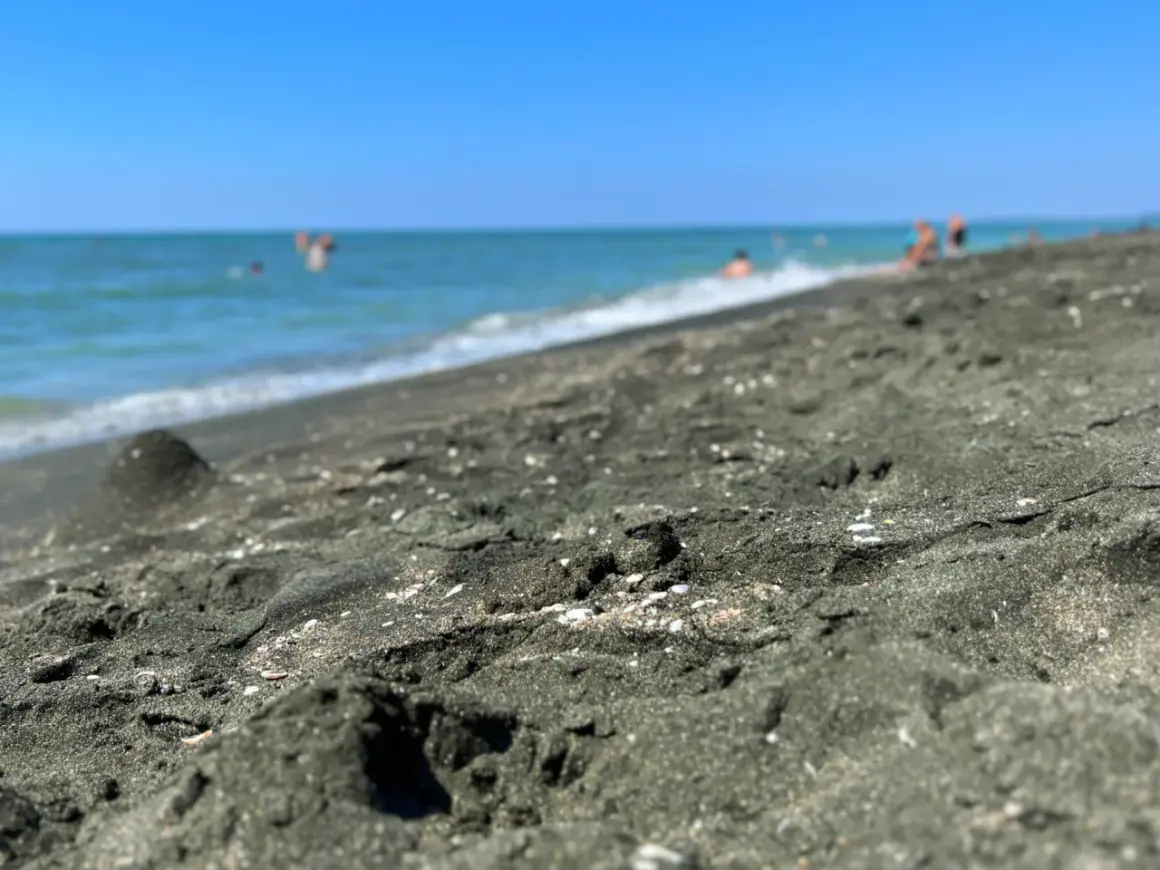 Ciemny piasek na plaży w Ureki, Gruzja. W tle widać turkusowe morze i kąpiących się ludzi.