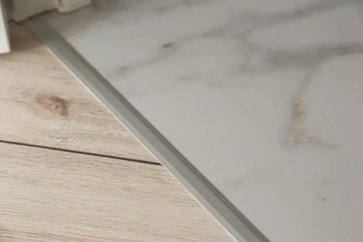 Un battiscopa in laminato effetto metallo separa un pavimento in finto marmo da uno in finto legno.