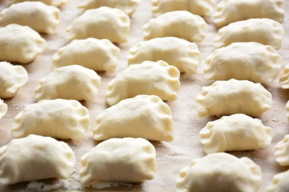 Gotowe do gotowania pierogi, przygotowane według tradycyjnego przepisu. Widać je ułożone rzędami na blacie.