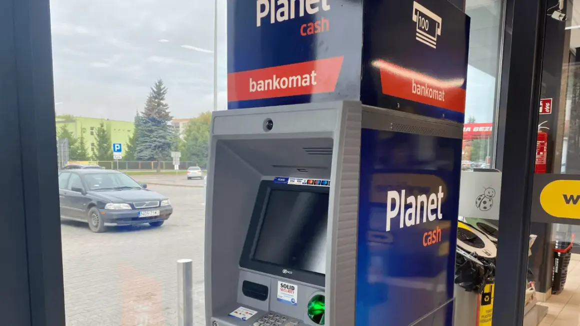 Bankomat Santander Planet Cash przy parkingu. Obok stoi czarny samochód.