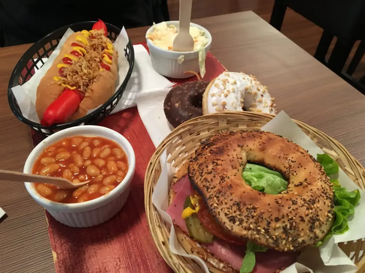 Un bagel de l'ouest garni de viande, salade et cornichons, accompagné d'un hot-dog, de haricots à la tomate, de salade de chou et de deux donuts.
