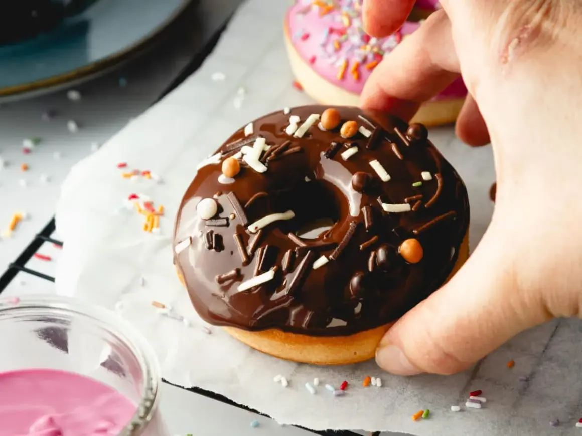 Leckeres Schoko-Donut-Rezept für den Backofen. Ein Donut mit Schokoglasur und Streuseln wird von einer Hand gehalten.