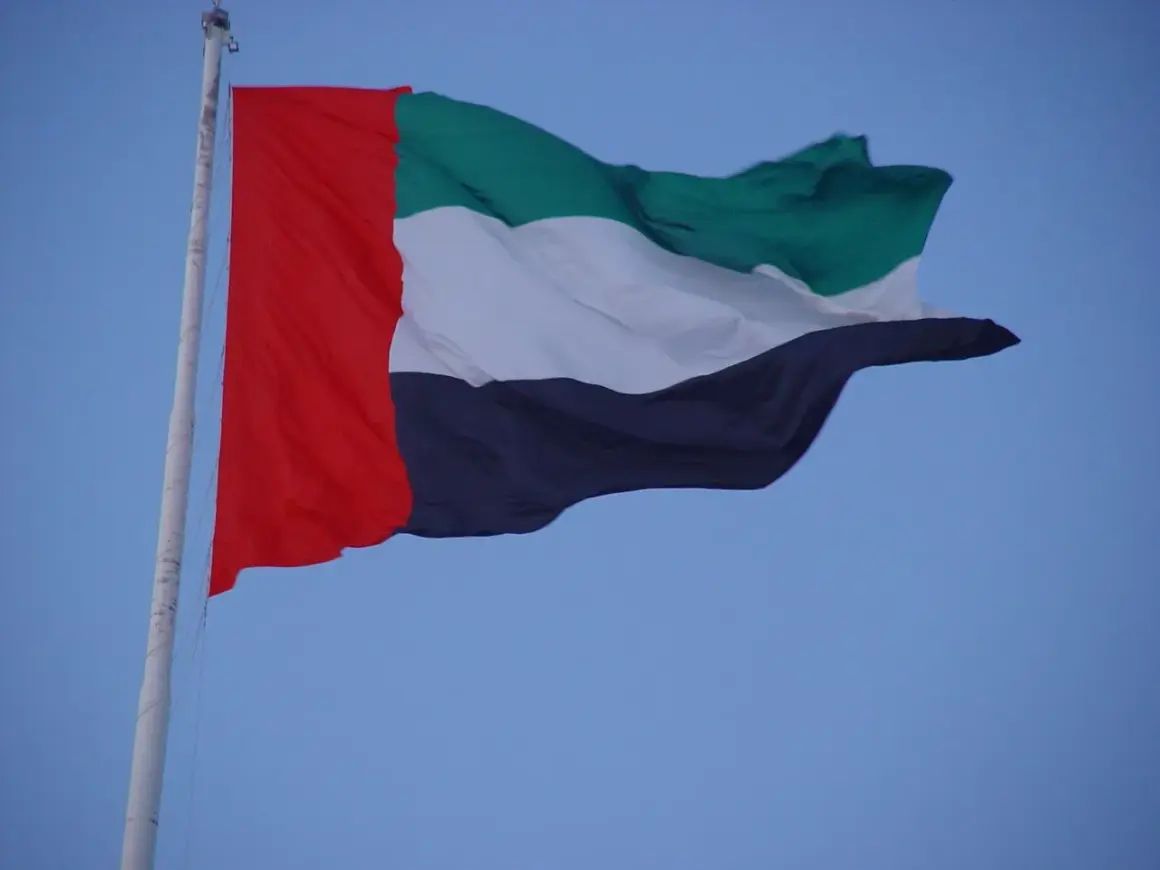 Flaga Zjednoczonych Emiratów Arabskich powiewa na maszcie na tle błękitnego nieba.